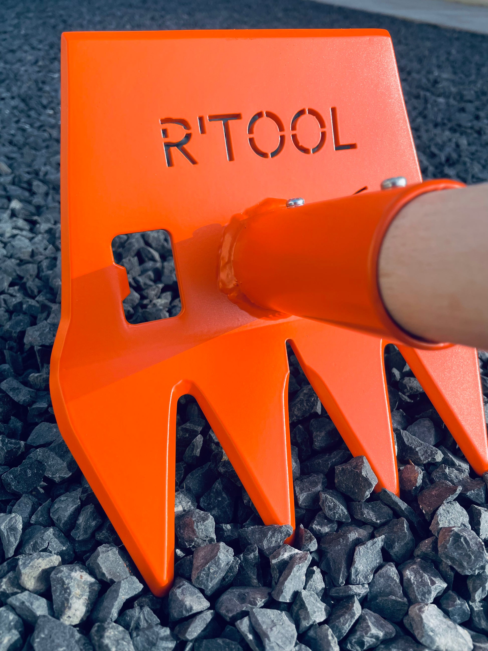 Close-up of R'TOOL Mini Shape'R trail building rake with wooden handle on gravel